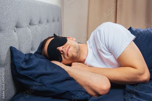 Top view of a young man wearing a sleep mask resting in his bedroom. Relaxation, rest after work.