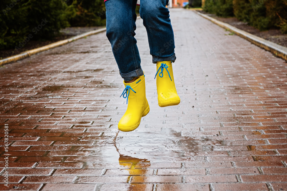 Jumping in puddle. Female legs in yellow rubber boots jumping on the puddle. Carefree young
