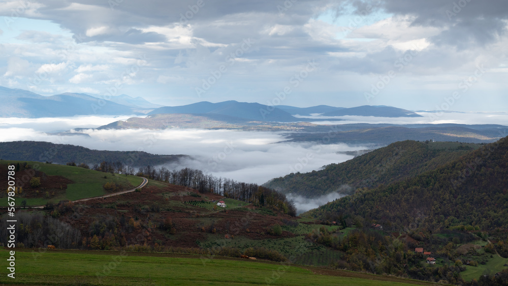 Mountain landscape with valley filled with fog and cloudy sky in morning, autumn season in mountains