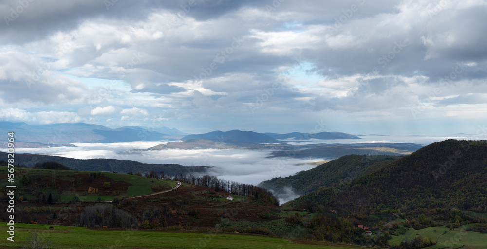 Mountain landscape with valley filled with fog and cloudy sky in morning, autumn season in mountains