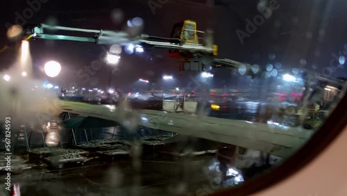 Aircraft de-icing before departure at night under snow storm. View of anti-icing spray application over the wing from inside the cabin window. photo