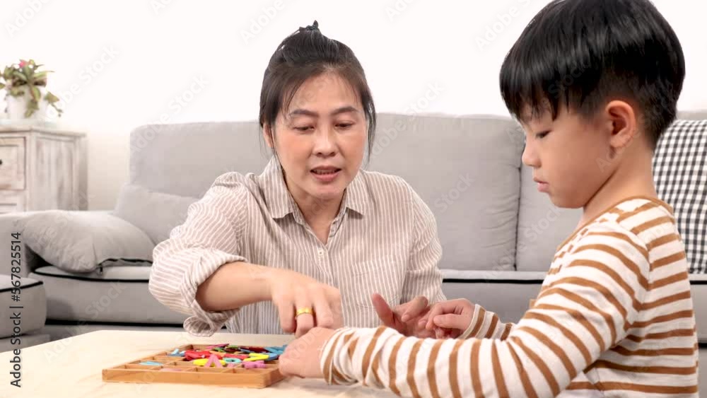 Asian happy single mother and handsome son playing alphabet games with plastic toys into the word with anxiously for improve mental health and memory. family spending time together in holiday.
