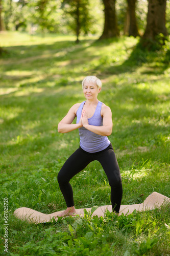 Middle-aged woman doing yoga in sportswear outdoors in a city park in Namaskarasana - Seated Prayer Pose. Concept of stretching, pilates, healthy lifestyle.