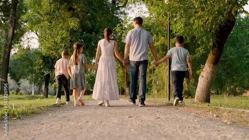 Big happy family walks in summer park holding hands. Family with children walks along sidewalk in an urban natural park. Family vacation, joy in nature. Healthy young family at sunset. Happy people