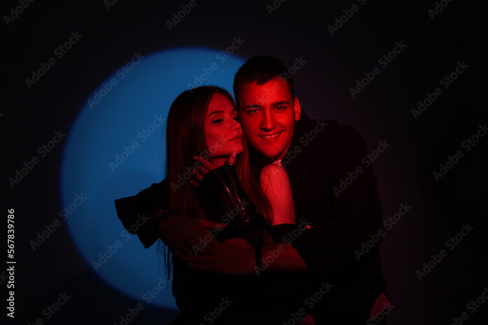 Happy handsome fashion couple man and woman with creative red light on dark background with circle blue light