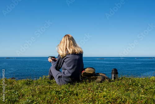 Woman with a cup of hot tea and a thermos sits on the ocean and admires the picturesque landscape. Beautiful nature. Harmony, relaxed lifestyle. Travel, adventure. Explore Northern Norway. Scandinavia