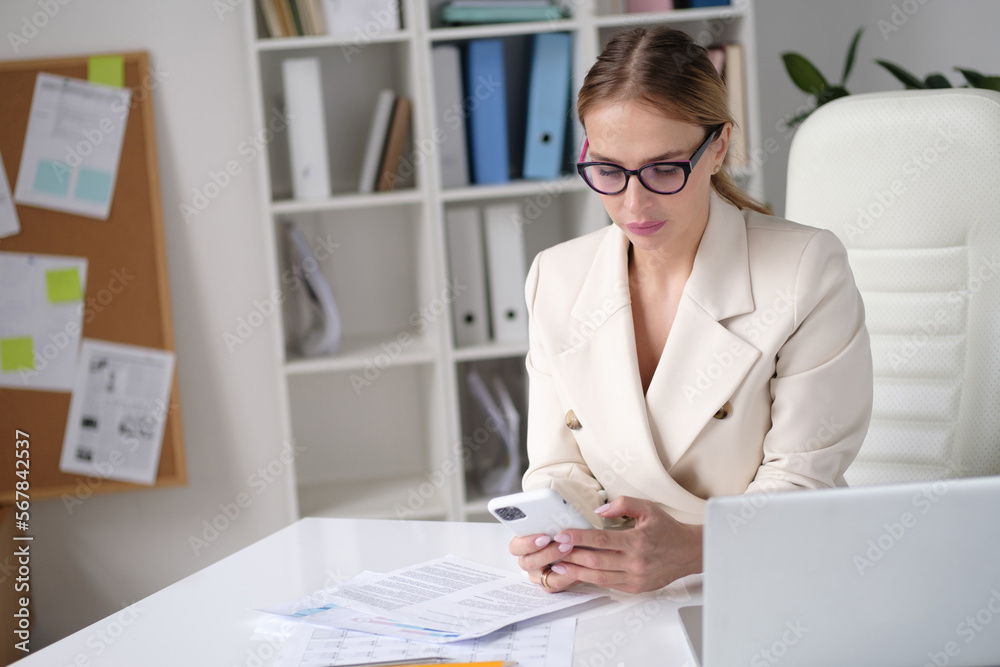 Happy businesswoman, sitting in her office and talking on mobile phone while analysing documents in her laptop. Happy businesswoman, sitting in her office and talking on mobile phone while analysing documents in her laptop.