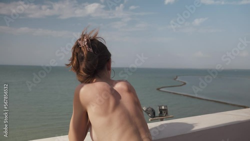 Young attractive girl without shirt contemplates the sea from a balcony at the beach in Cadiz, Andalucia, Spain.She enjoys the sun on holidays.