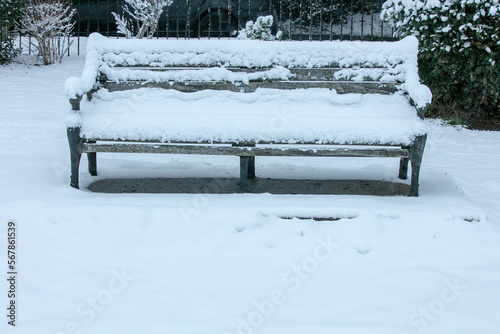 Closeup of a bench in a park  covered in snow on a cold day.