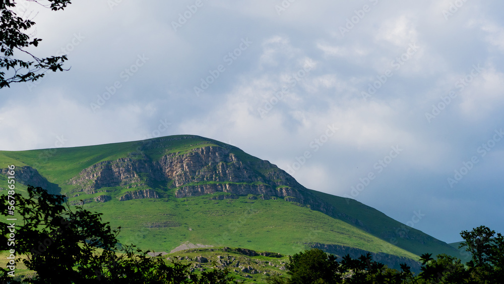 Fototapeta premium Rocky hill with grass on the surface, huge white clouds over the top , laconic landscape
