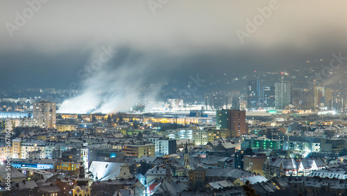 Cityscape of Graz at night with buildings and smoking plants in far distance