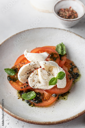 Caprese salad in modern feed with tomatoes, basil, mozzarella, pesto. Traditional Italian food on white background close up, menu