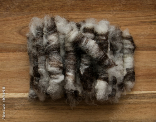 A stack of small brown and white rolags made of sheep's wool, ready for spinning, against a wooden background.