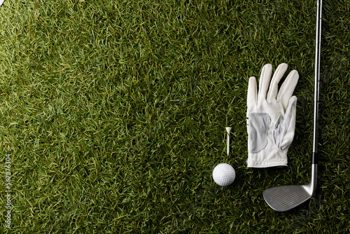 White glove, tee, golf ball and golf club on grass with copy space