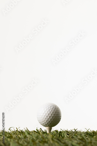 Close up of white golf ball on tee on grass with copy space on white background