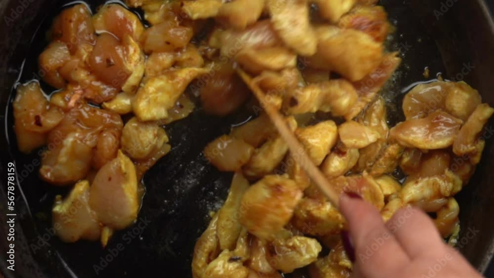 Top view of a wooden spatula spoon stires juicy chicken pieces on the hot pan Top view of a wooden spatula spoon stires juicy chicken pieces on the hot pan