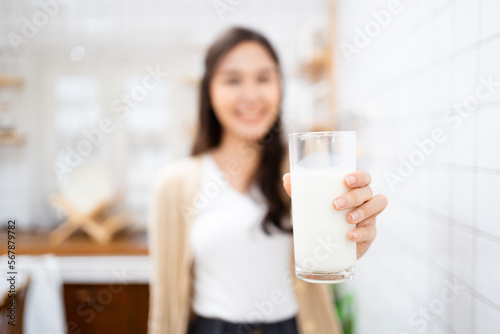 Beautiful happy Asian woman drinking a milk in morning in kitchen and smiling to camera.