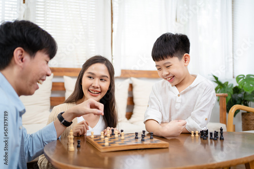 Happy Asian lovely family staying and playing a chess game together in living room in weekend, Group of Asian people playing chess game together in.