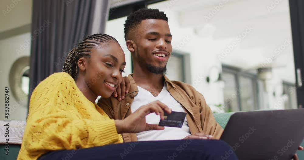 Happy african american couple sitting on sofa and making online shopping