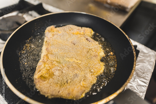 Frying breaded pork cutlet schabowy in oil in a frying pan. Restaurant kitchen food preparation process. Horizontal indoor shot. High quality photo