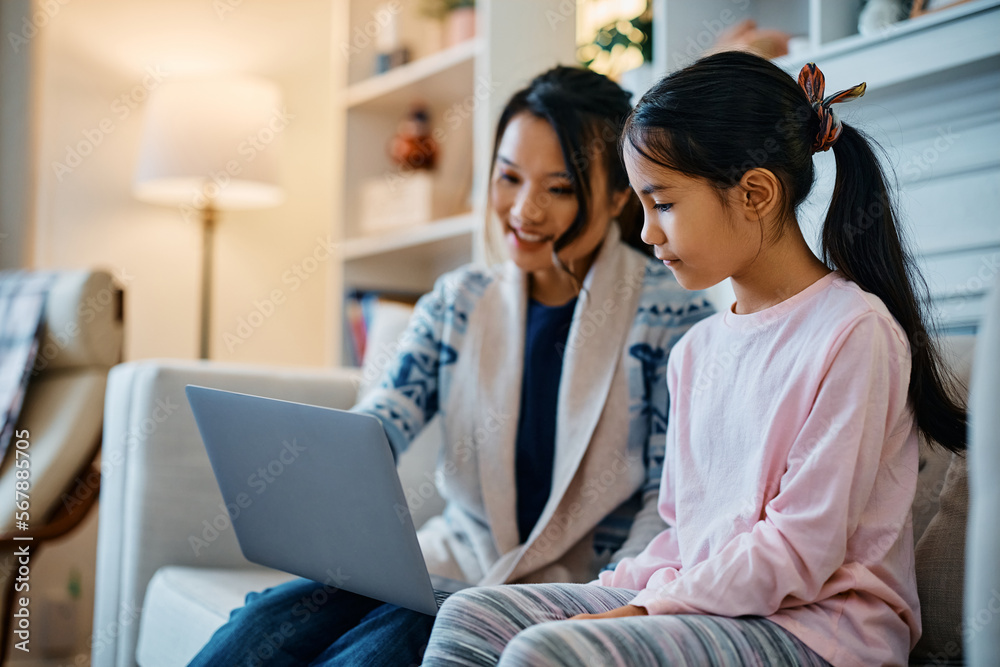 Asian mother and daughter surfing the net on laptop while relaxing at home.