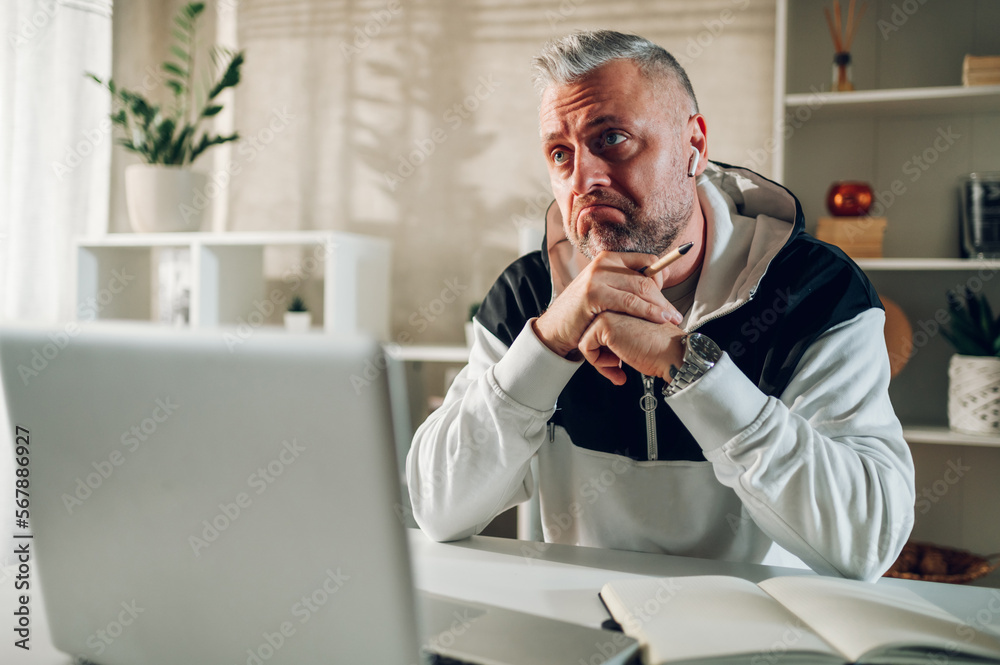 Fototapeta premium Sad middle aged man using a laptop while working in a home office