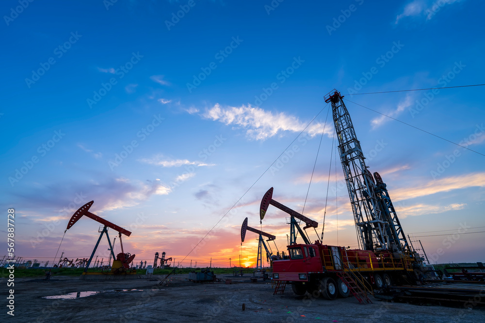 in the evening, oil pumps are running, The oil pump and the beautiful sunset reflected in the water, the silhouette of the beam pumping unit in the evening.