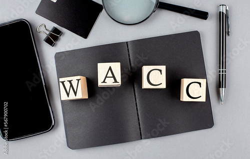 Word WACC on wooden block on black notebook with smartpone, credit card and magnifier photo