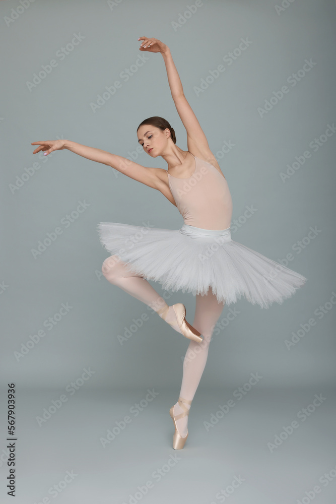 Fototapeta premium Young ballerina practicing dance moves on light grey background