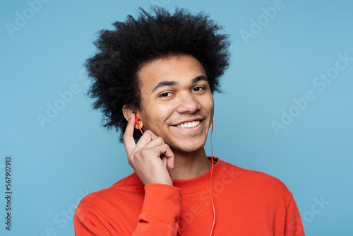 Authentic portrait of attractive smiling African American man listening music in red earphones looking at camera isolated on colorful background. People and emotions concept