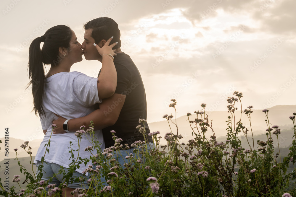Young couple in love hugging and kissing in a natural environment with flowers. Couple giving each other affection and love in the mountains with sunset in the background. Young couple in love hugging and kissing in a natural environment with flowers. Couple giving each other affection and love in the mountains with sunset in the background.