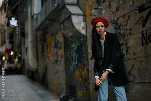 Fashion woman portrait walking tourist in stylish clothes with red lips walking down a narrow city street, travel, cinematic color, retro vintage style, dramatic against a wall with graffiti.