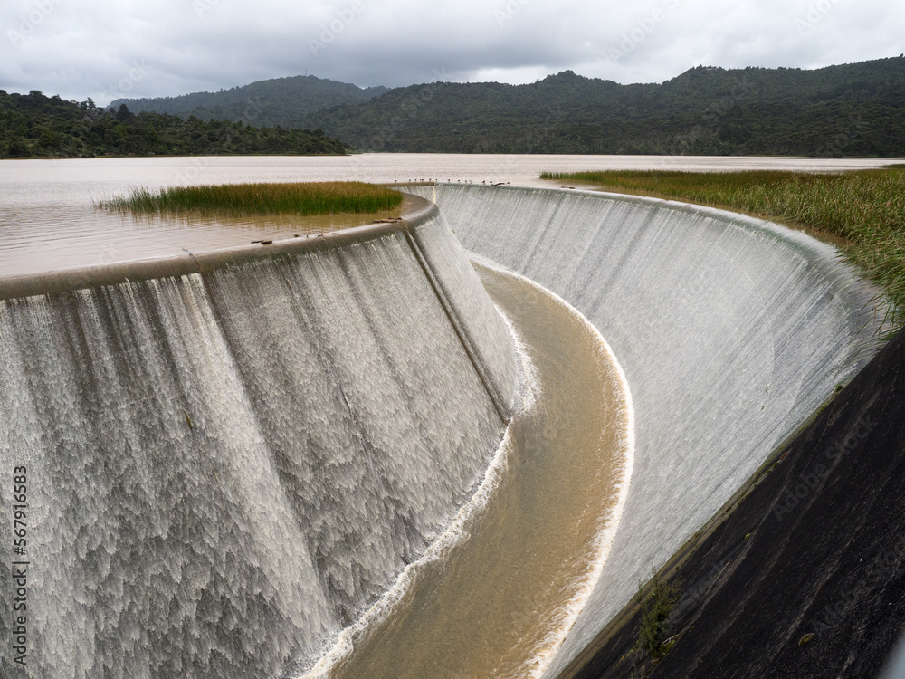 Lower Nihotupu Reservoir shows water cascading and overflowing the side walls due to record breaking heavy rainfall in New Zealand.Waitakere.