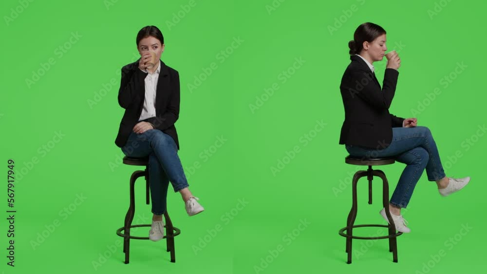 Female manager drinking cup of coffee before working at office, sitting on chair in suit. Corporate employee enjoying caffeine beverage in studio, posing over full body green screen.