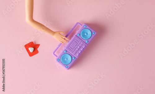 Doll's hand holding Miniature boombox tape recorder with Social media like on pink background. Creative minimal layout