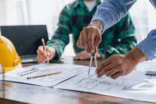 Engineers consulting team close up to design building blueprints paper for clients with building models to work at office.