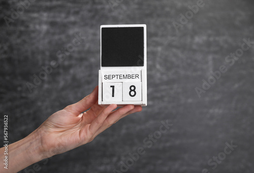Wooden block calendar with date september 18 in female hand on background of school chalk blackboard