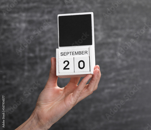 Wooden block calendar with date september 20 in female hand on background of school chalk blackboard