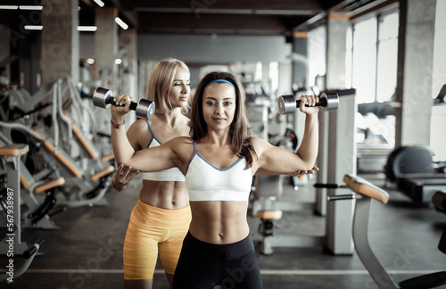 Fit woman and her trainer doing exercise at the gym. Personal trainer coordinates woman working with heavy dumbbells