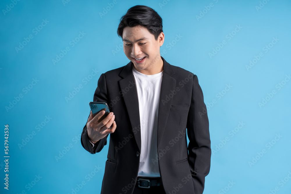 Young business man wearing a vest using phone and posing on a blue background Young business man wearing a vest using phone and posing on a blue background