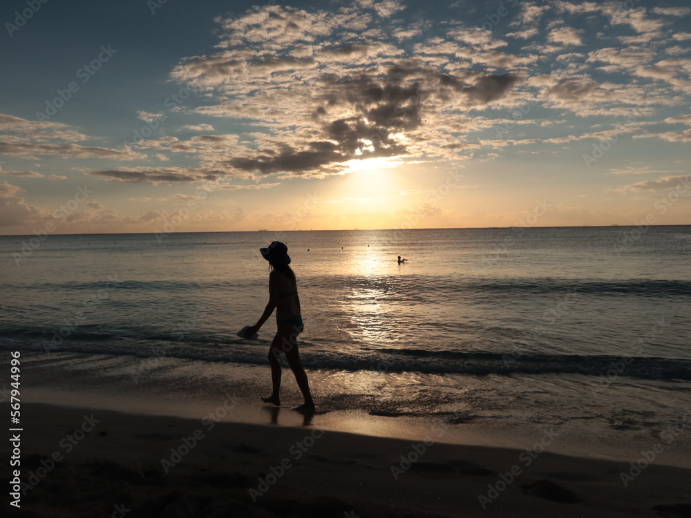 Amanecer en una playa del caribe con mar tranquilo, sol saliendo y gente empezando a caminar.
