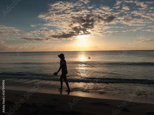 Amanecer en una playa del caribe con mar tranquilo, sol saliendo y gente empezando a caminar.