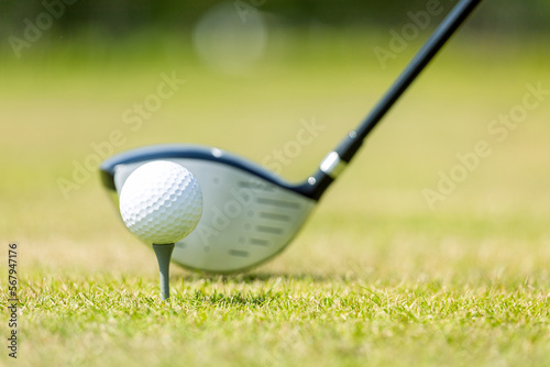 White golf ball on the stand on a green field, putter on the background