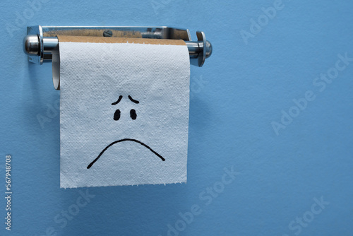 Close-up sad face on the last piece of toilet paper tissue on a brown cardboard toilet roll blue wall copy space