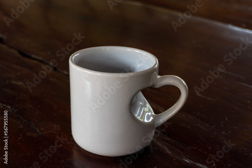 Love in the Morning: A White Mug with Heart Shaped Handle on Wooden Table © dendyh7