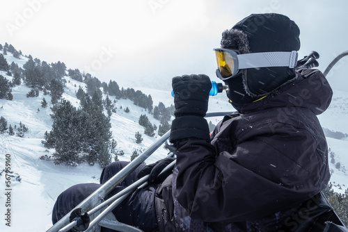 Skier exhausted and drinking water from a bottle while climbing the ski slopes on the chairlift.