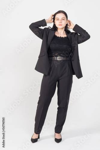 A young brunette poses standing on a white background / The girl is dressed in a strict business suit, there is a lot of space around the model for copyspace