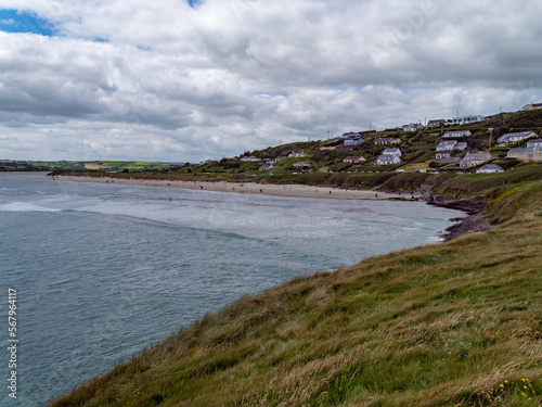 View of Inchydoney beach from the Cape of the Virgin Mary. Irish seascape. A small European settlement on the seashore in summer. Green grass near body of water under cloudy sky