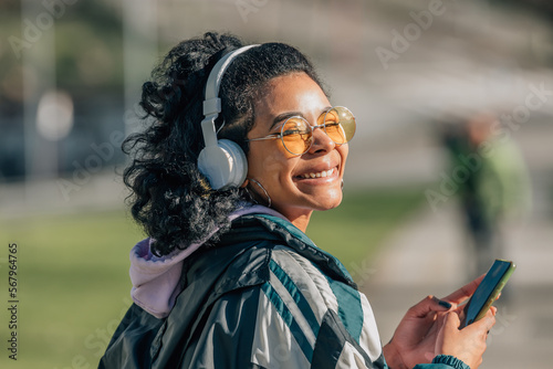 girl on the street with headphones and mobile phone smiling looking at camera