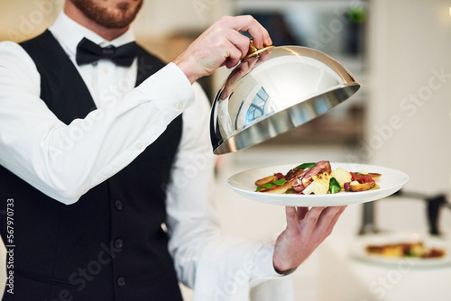 Waiter, hands and opening plate of food for serving, meal or customer service at indoor restaurant. Man employee caterer or server catering or bringing open dish for fine dining, hospitality or order photo